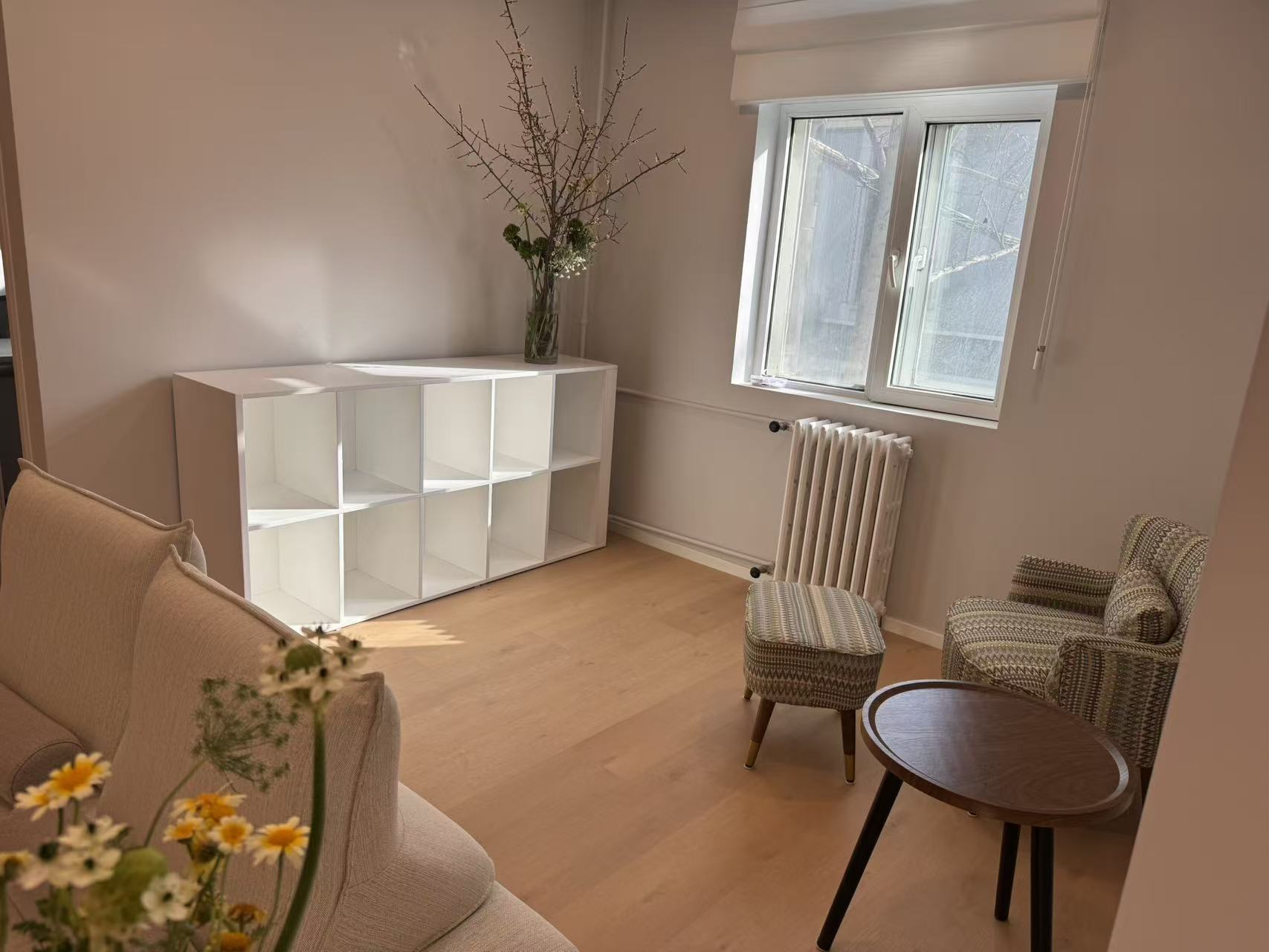 Warm beige sitting room with armchairs, a small wooden table and fresh branches by the window
